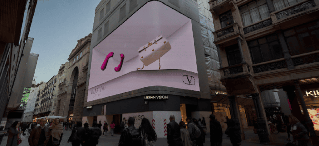Un cartellone digitale che mostra la pubblicità di Valentino in mezzo agli edifici 